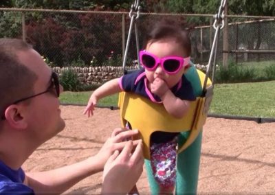 Toddler with pink, 70's style sunglasses being gently pushed on a swingset
