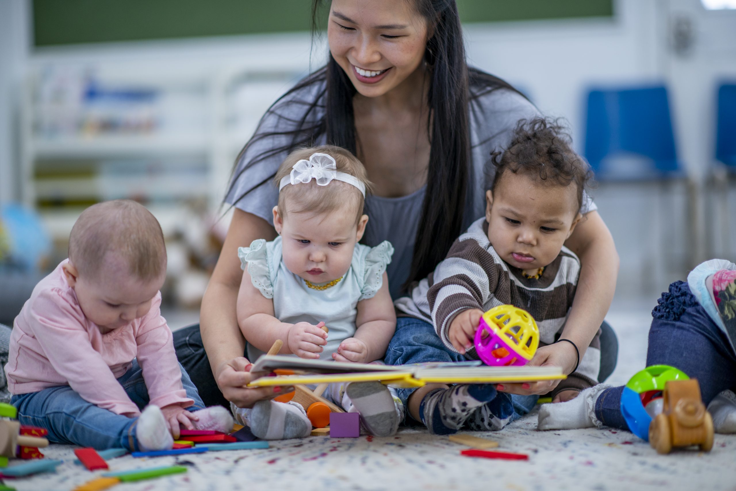 Daycare Worker Sitting on the Floor Reading to Babies stock photo child care classroom