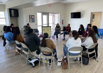 About a dozen parents sit in a circle in a community room, holding strands of yarn stretched between them into a web.