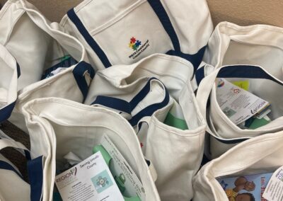 Canvas tote bags printed with the PIECE Coalition logo, filled with board books, bibs, and family resource flyers.