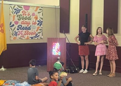 Children sit on the floor at a reading event beneath a banner reading "It's a Good Day to Read a Book."